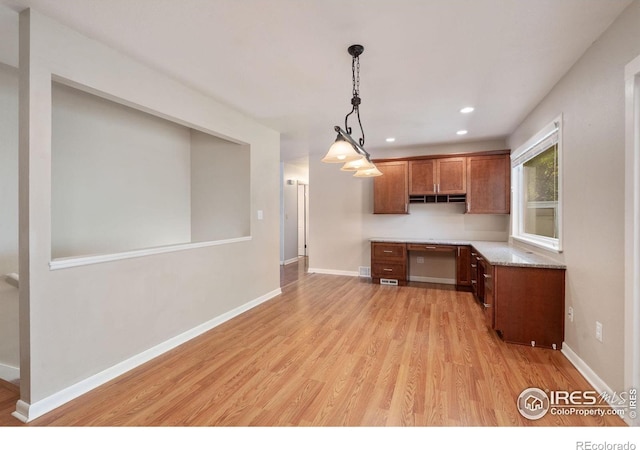 kitchen featuring light wood-type flooring, light stone counters, built in desk, and pendant lighting