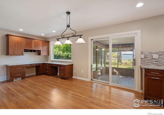 kitchen with light stone counters, built in desk, hanging light fixtures, and light hardwood / wood-style floors