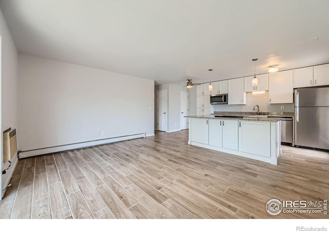 kitchen with white cabinets, hanging light fixtures, a kitchen island, appliances with stainless steel finishes, and light hardwood / wood-style floors