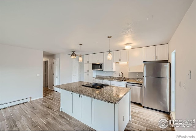 kitchen with light wood-type flooring, a kitchen island, white cabinetry, stainless steel appliances, and dark stone counters