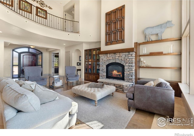 living room with a stone fireplace, light hardwood / wood-style floors, and a high ceiling