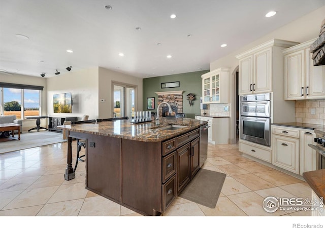 kitchen featuring decorative backsplash, a breakfast bar, sink, dark stone counters, and a fireplace