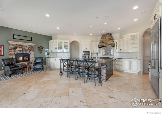 kitchen featuring dark stone countertops, a kitchen island with sink, a kitchen bar, and decorative backsplash