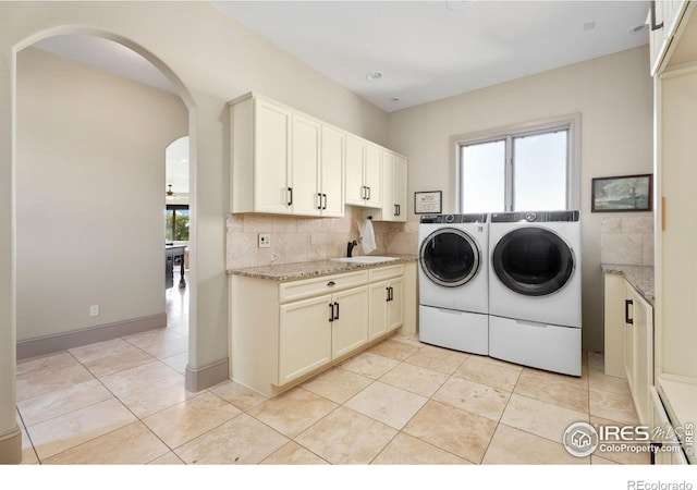 laundry area featuring independent washer and dryer, cabinet space, arched walkways, and light tile patterned flooring