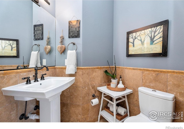 half bathroom featuring tile walls, toilet, and wainscoting