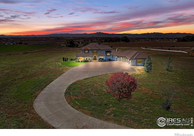 view of front of property featuring a mountain view, curved driveway, and a lawn