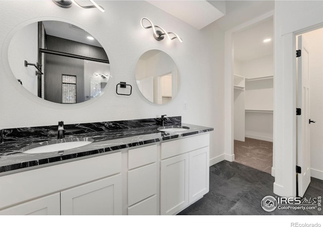 bathroom featuring a spacious closet, double vanity, baseboards, and a sink