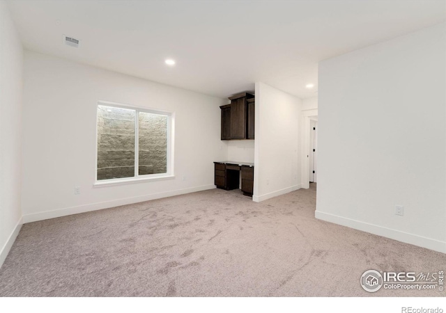 unfurnished living room with light carpet, recessed lighting, built in study area, and baseboards