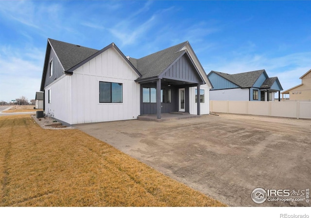 view of front of property featuring a front lawn, a patio, fence, board and batten siding, and roof with shingles