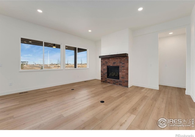 unfurnished living room with visible vents, a brick fireplace, baseboards, light wood-type flooring, and recessed lighting