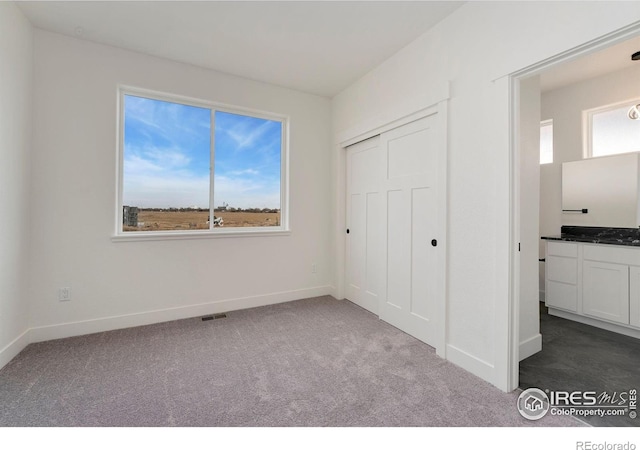 unfurnished bedroom with dark colored carpet, visible vents, baseboards, and a closet