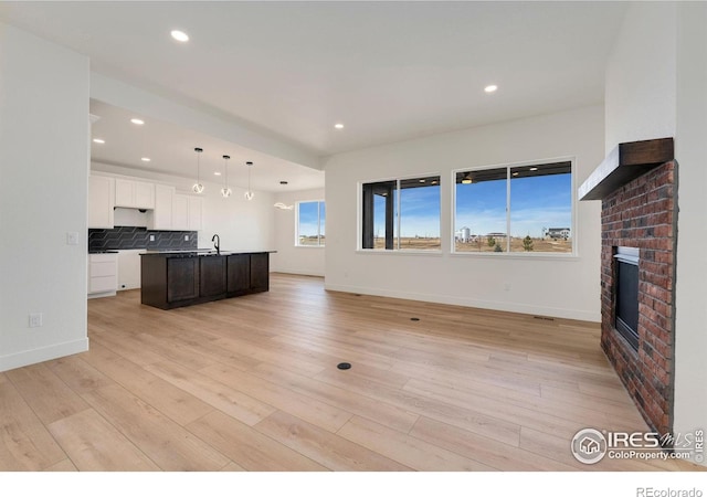 unfurnished living room featuring a sink, recessed lighting, a fireplace, light wood finished floors, and baseboards