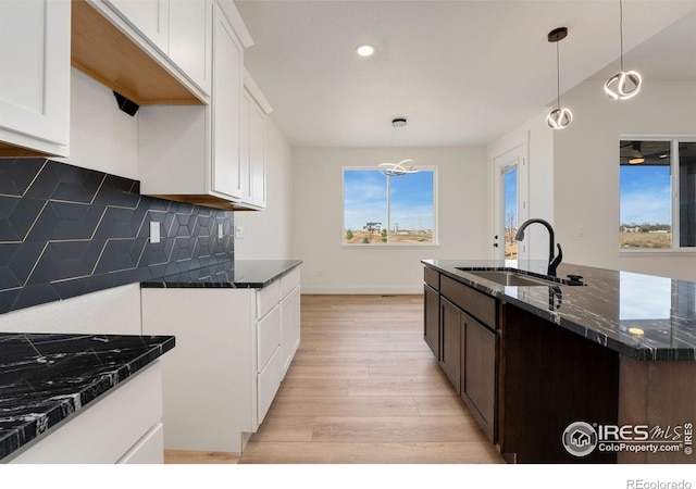 kitchen featuring tasteful backsplash, light wood finished floors, dark stone counters, and a sink