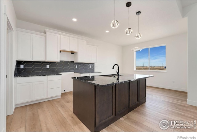 kitchen featuring a sink, white cabinetry, dark stone counters, light wood-style floors, and decorative backsplash