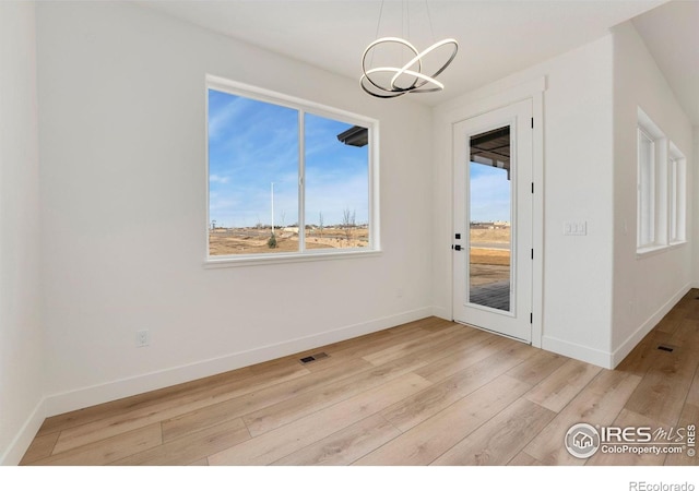 interior space featuring light wood-type flooring, visible vents, baseboards, and a notable chandelier