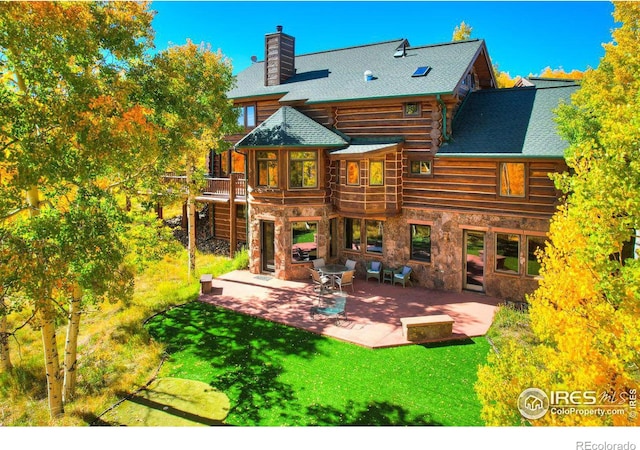 rear view of property with a yard, stone siding, a chimney, and a patio area