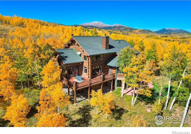 rear view of house with a wooded view, log exterior, a mountain view, and a chimney