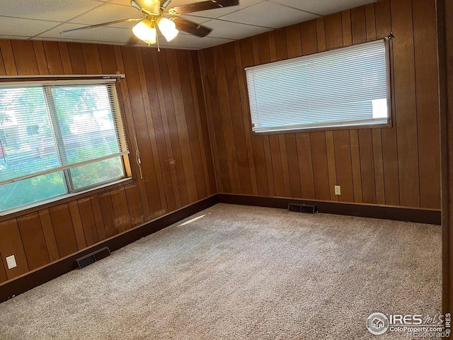 carpeted spare room featuring ceiling fan, wooden walls, and a paneled ceiling