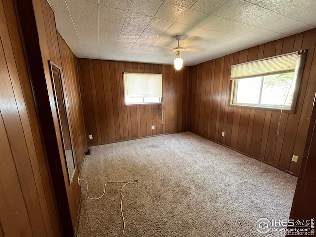 empty room featuring wood walls, ceiling fan, carpet floors, and a healthy amount of sunlight