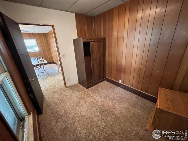 carpeted empty room featuring wood walls and a drop ceiling