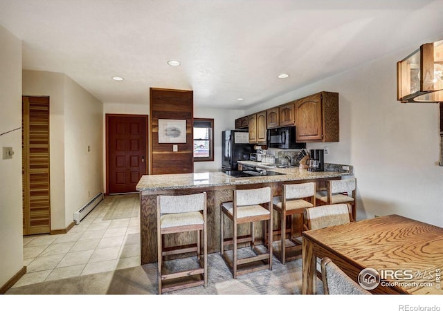 kitchen featuring black appliances, kitchen peninsula, a breakfast bar area, light tile patterned floors, and baseboard heating