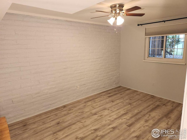 unfurnished room featuring brick wall, hardwood / wood-style flooring, and ceiling fan