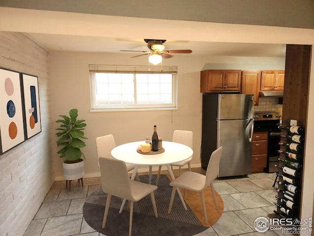 dining area featuring light tile patterned floors, ceiling fan, and brick wall