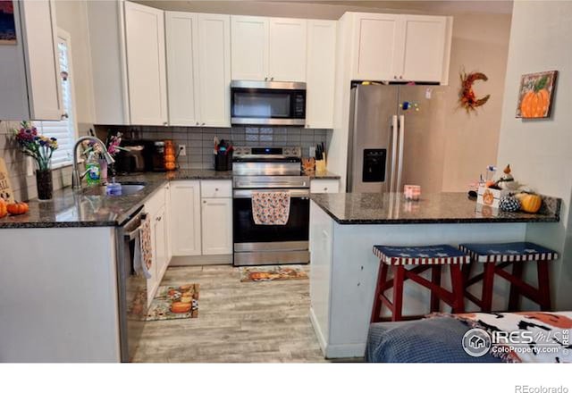 kitchen featuring stainless steel appliances, dark stone countertops, sink, white cabinetry, and light hardwood / wood-style flooring