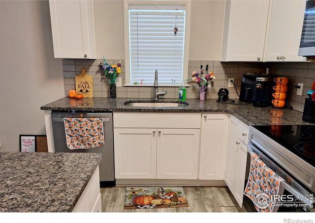 kitchen featuring appliances with stainless steel finishes, dark stone countertops, sink, and white cabinets