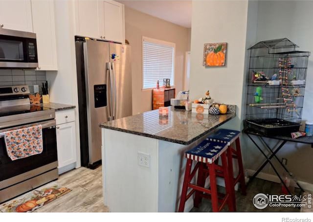 kitchen featuring stainless steel appliances, kitchen peninsula, a breakfast bar, and white cabinetry