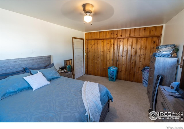 carpeted bedroom featuring ceiling fan and wooden walls