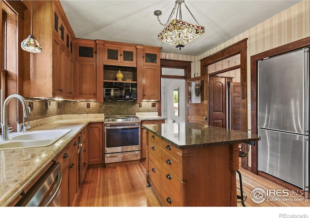 kitchen featuring a kitchen island, light stone countertops, sink, light hardwood / wood-style flooring, and appliances with stainless steel finishes