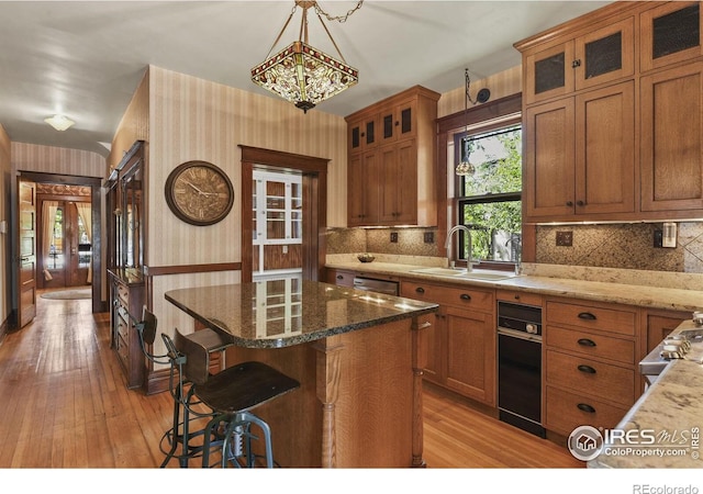 kitchen featuring a kitchen island, light stone counters, light wood-type flooring, sink, and hanging light fixtures