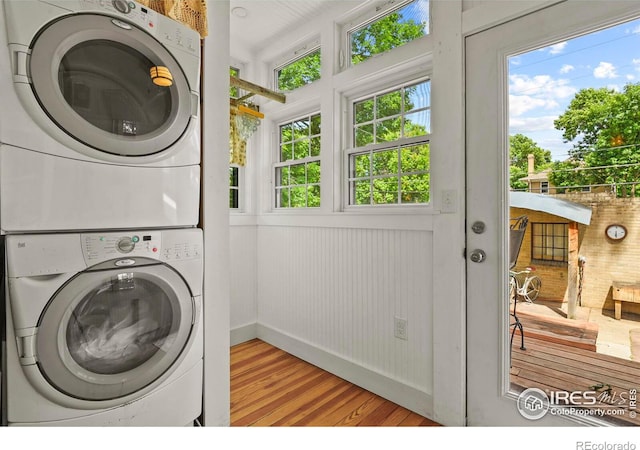 clothes washing area featuring light hardwood / wood-style flooring, plenty of natural light, and stacked washer and dryer