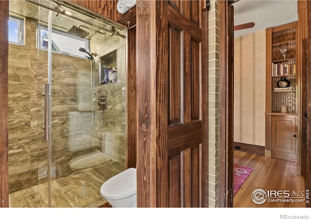 bathroom featuring hardwood / wood-style flooring, a shower with shower door, and toilet