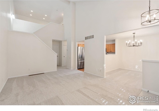 unfurnished living room featuring a high ceiling, light colored carpet, and an inviting chandelier