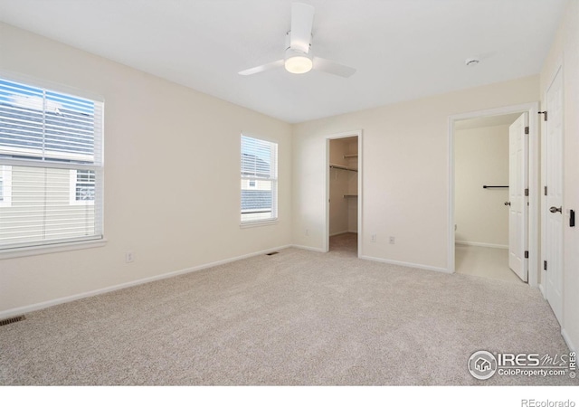 unfurnished bedroom featuring light carpet, ceiling fan, a closet, and a walk in closet