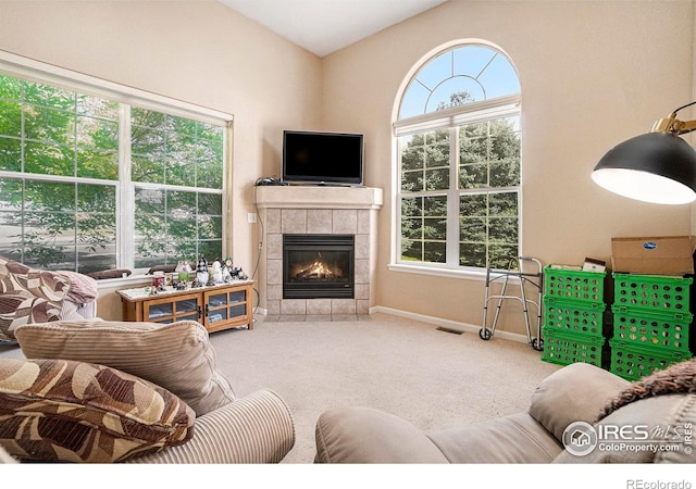 carpeted living room featuring a tile fireplace, vaulted ceiling, and a healthy amount of sunlight