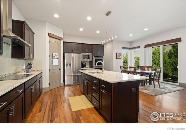 kitchen featuring a center island with sink, hardwood / wood-style flooring, wall chimney exhaust hood, and stainless steel appliances