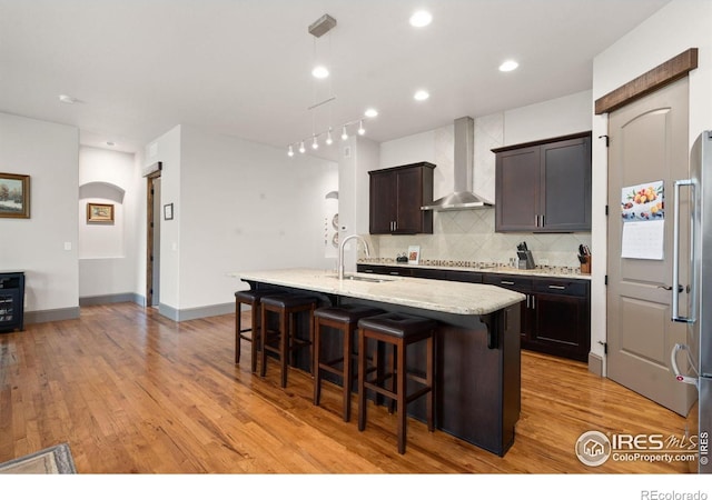 kitchen featuring a kitchen island with sink, sink, wall chimney range hood, a breakfast bar area, and light hardwood / wood-style flooring