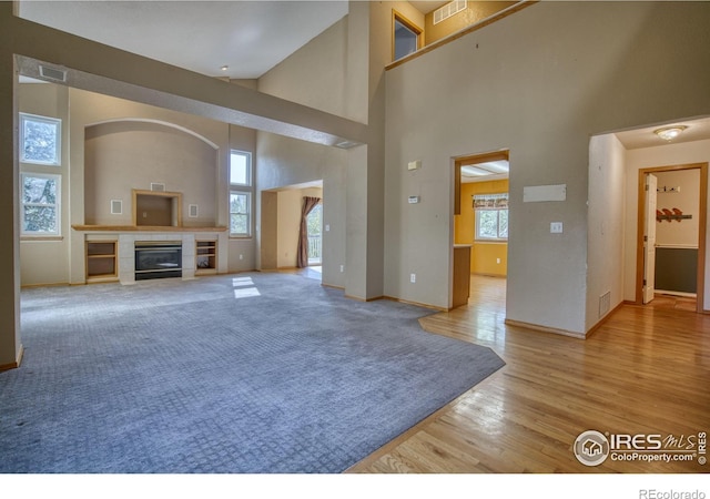 living room with light hardwood / wood-style flooring, a tiled fireplace, and a high ceiling