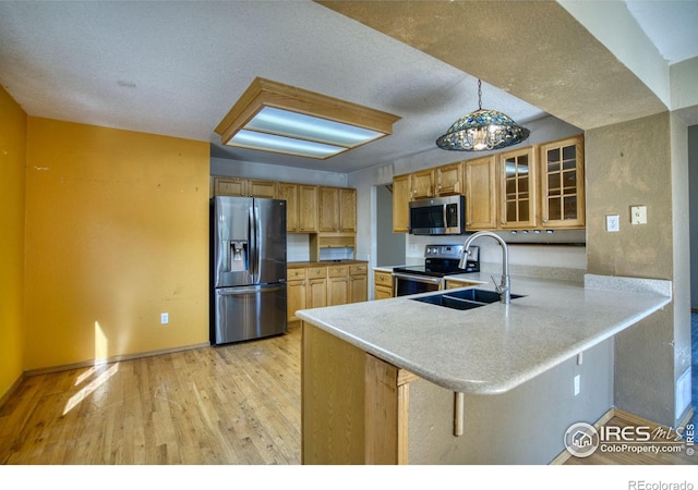 kitchen featuring pendant lighting, kitchen peninsula, appliances with stainless steel finishes, a kitchen breakfast bar, and light hardwood / wood-style floors