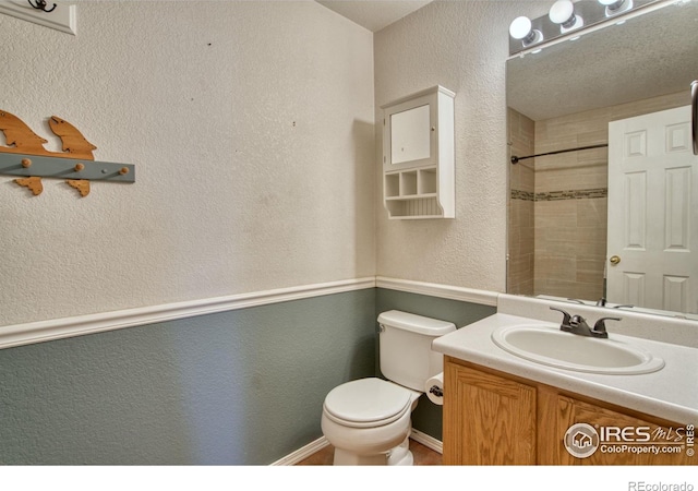 bathroom with a textured ceiling, a tile shower, vanity, and toilet