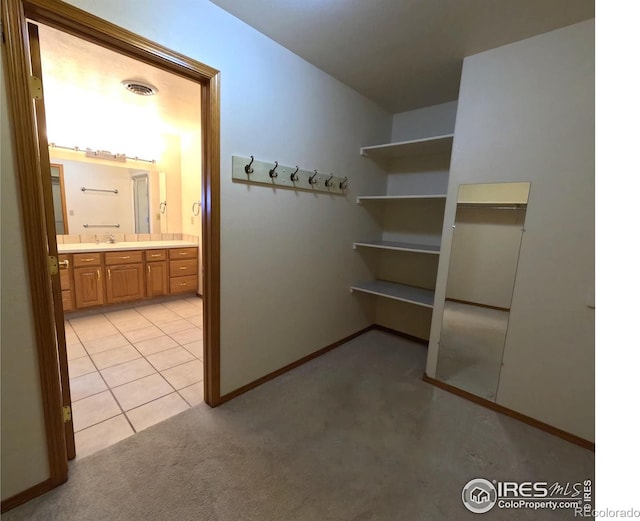 hall featuring light tile patterned floors, baseboards, visible vents, a sink, and light colored carpet