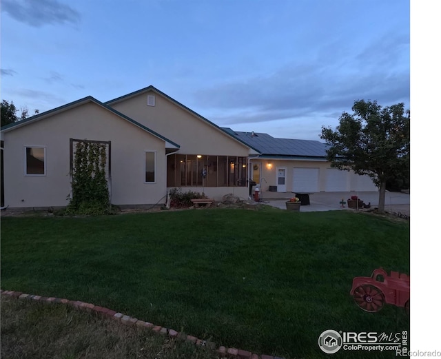 rear view of property featuring a lawn, stucco siding, driveway, a sunroom, and an attached garage