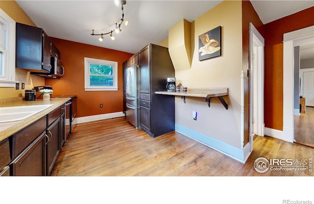 kitchen with appliances with stainless steel finishes, sink, dark brown cabinets, and light hardwood / wood-style floors