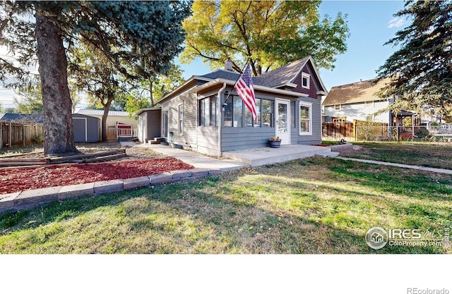 bungalow featuring a storage unit, a front lawn, and a patio