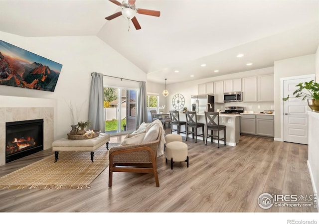 living room with ceiling fan, a fireplace, high vaulted ceiling, and light hardwood / wood-style floors