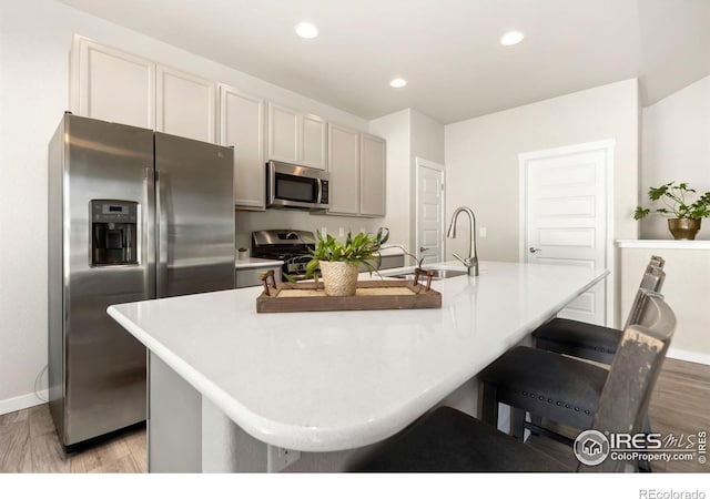 kitchen featuring a kitchen island with sink, sink, light wood-type flooring, and appliances with stainless steel finishes