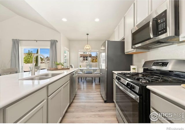 kitchen with sink, light hardwood / wood-style floors, decorative light fixtures, vaulted ceiling, and appliances with stainless steel finishes